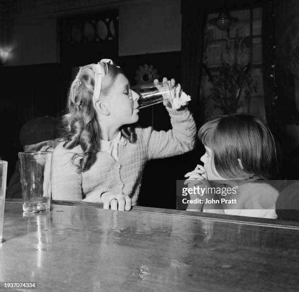 Two young girls sitting at the bar of the Royal George pub in Rotherhithe, London, November 1954. On Sunday afternoons, pub landlord Bill Barritt...
