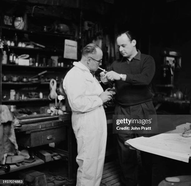 British racing driver Donald Campbell lights chief mechanic Leo Villa's cigarette in the workshop at his home near Betchworth, Surrey, November 1954....