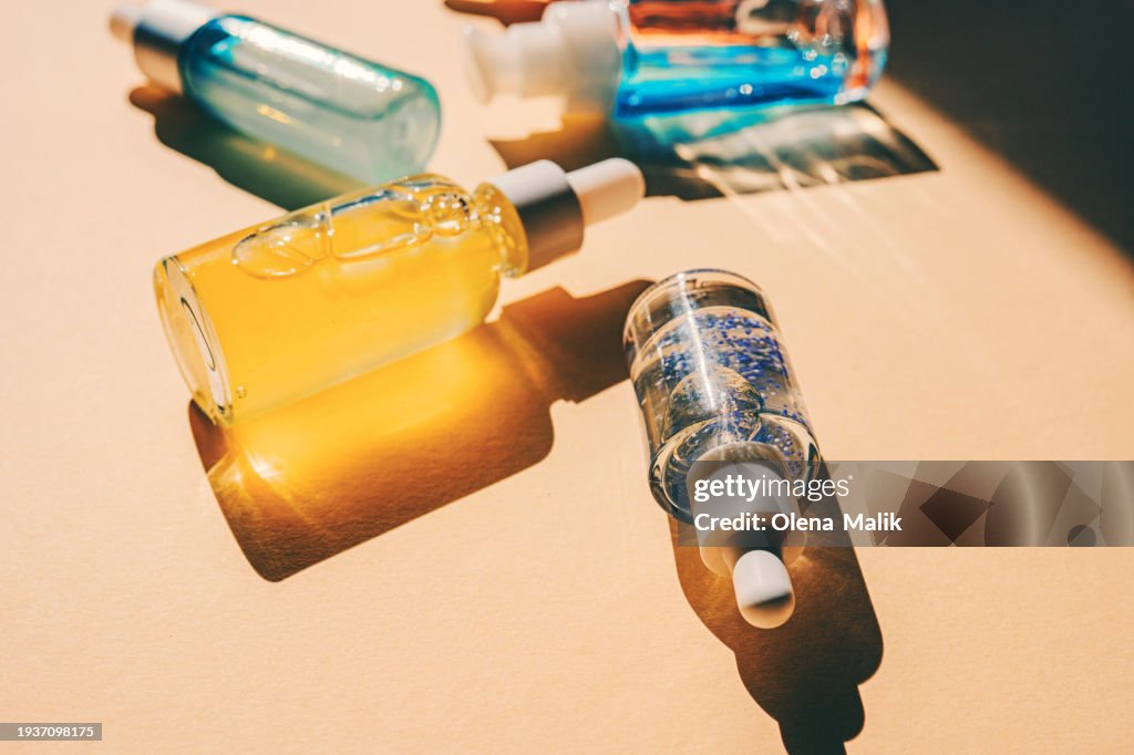 Assorted glass bottles with cosmetic liquids, serum or gel. Vibrant trendy background of cosmetic products, flat lay style