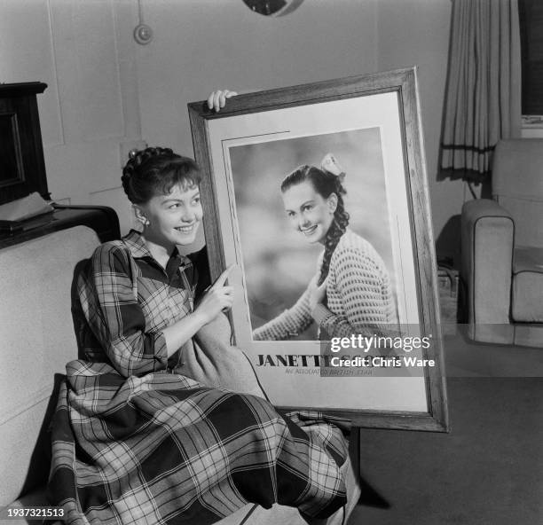 British actress Janette Scott, wearing a plaid dress, holding a large framed portrait of herself, with the caption 'An Associated British Star', at...