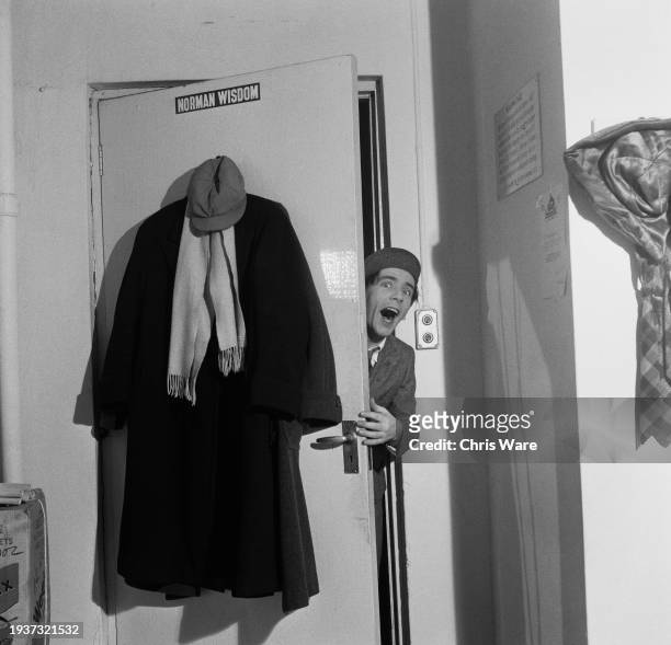 British comedian, actor and singer Norman Wisdom, emerges from behind the door to his dressing room, backstage at the London Palladium, in the West...