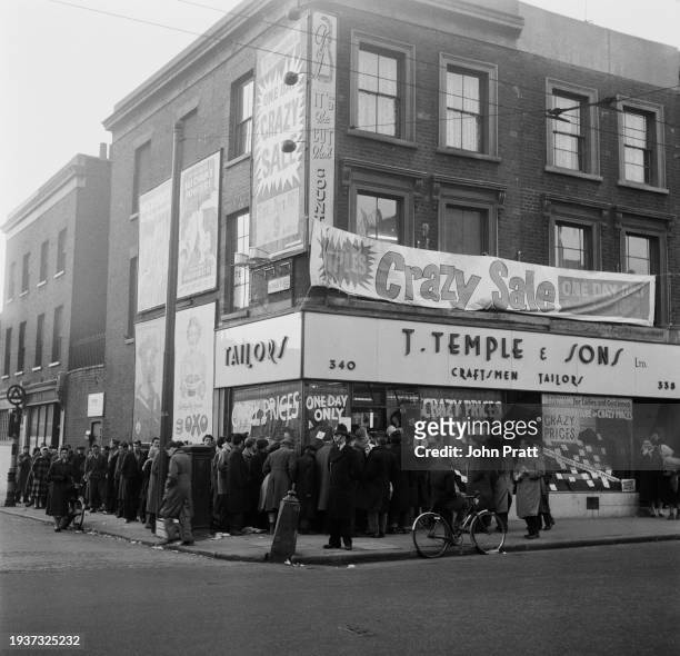 Crowds line the street outside J Temple & Sons tailors, a banner reads 'Crazy Sale' as the store held a sale, on Hackney Road in Hackney, London,...