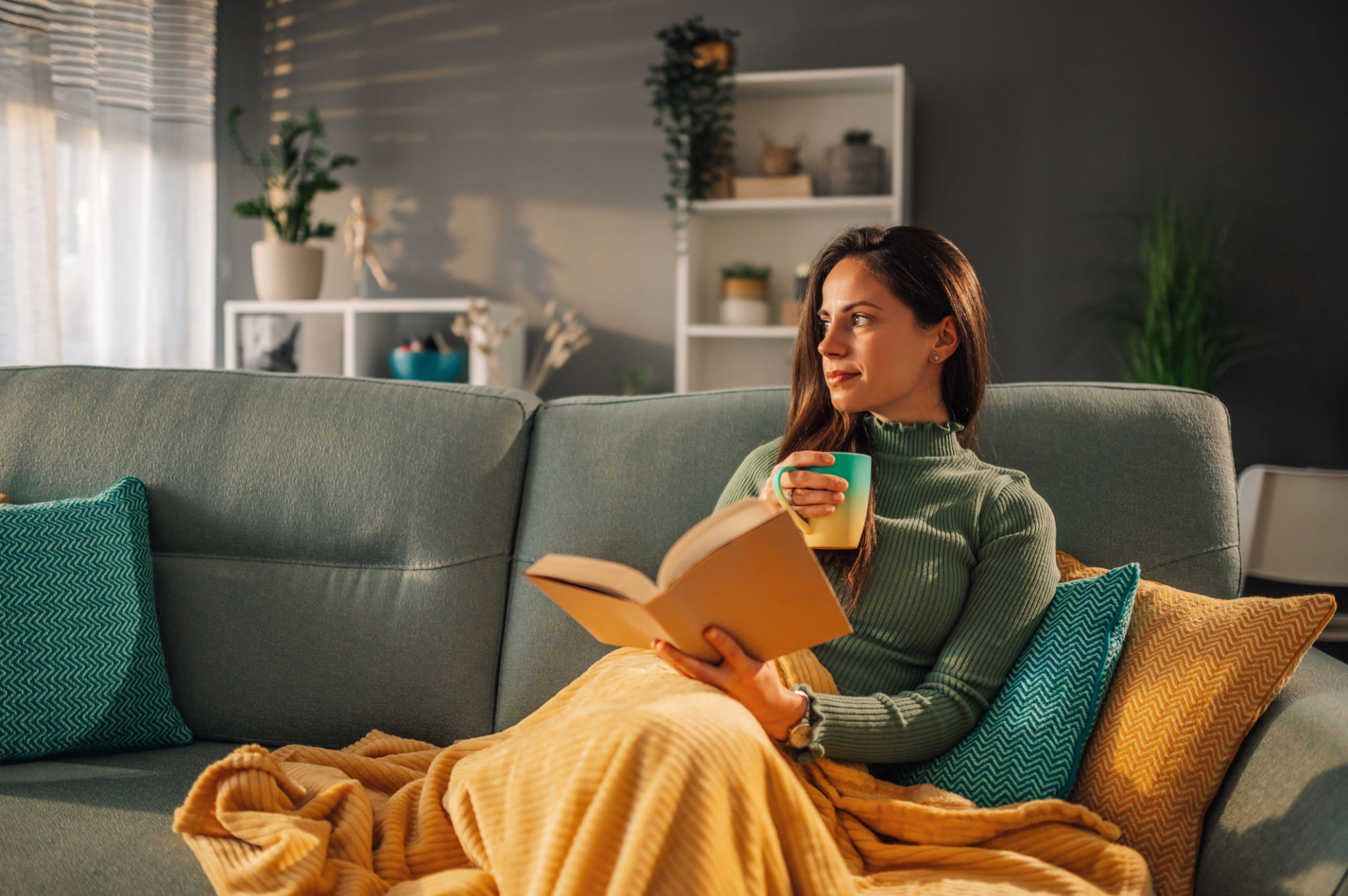 Woman sitting on comfy couch reading a book and drinking coffee or tea Woman sitting on comfy couch reading a book and drinking coffee or tea