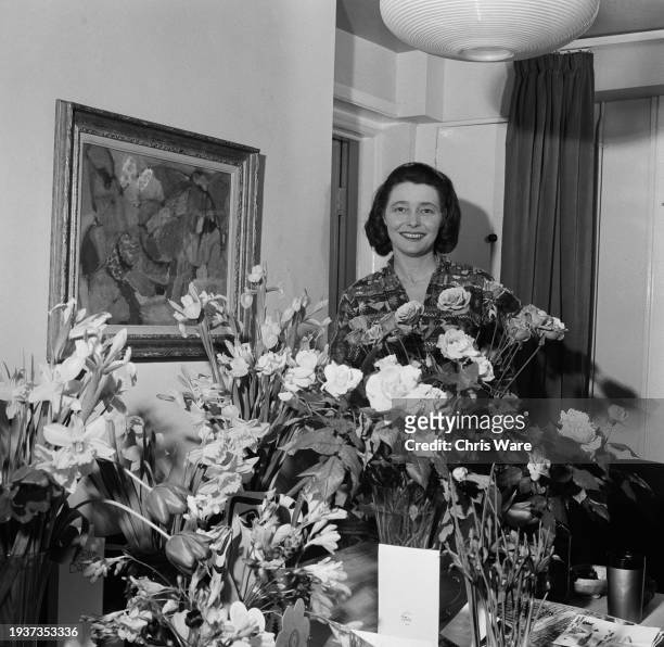 American actress Patricia Neal stands behind floral arrangements sent to her by well-wishers following a period of ill-health, at her home, Gipsy...
