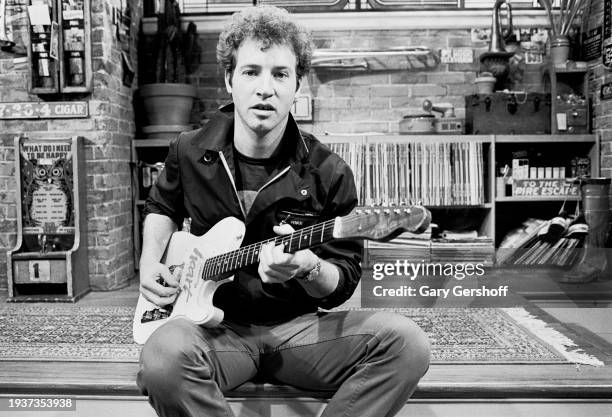 View of American Pop musician Tommy Heath, of the band Tommy Tutone, plays an electric guitar as he sits on a low stage following an interview on MTV...