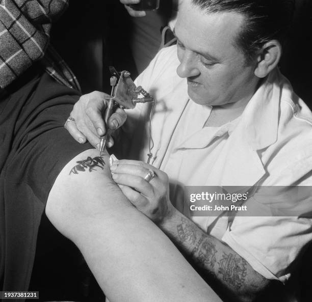 Tattooist Les Skuse tattoos the badge of the Bristol Tattoo Club onto the leg of a woman at a club meeting in Bristol, England, October 1954. Also...