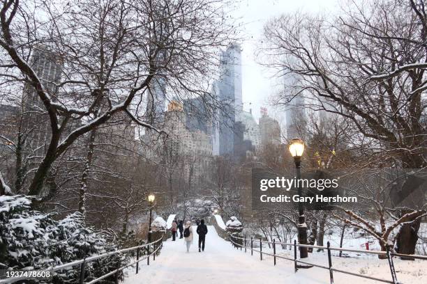 People walk over the Gapstow Bridge as snow falls in Central Park on January 16, 2024 in New York City. The City received a rare accumulation of snow...