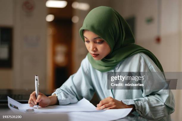 nahaufnahme einer schönen jungen studentin, die hijab trägt und eine hausarbeit in der schule schreibt - indonesian ethnicity stock-fotos und bilder