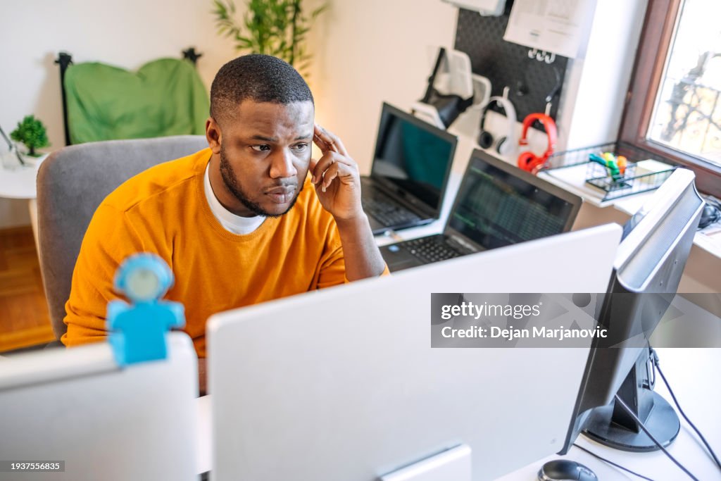 Programmer sitting in front of computer screens and working as a freelancer at home settings looking worried