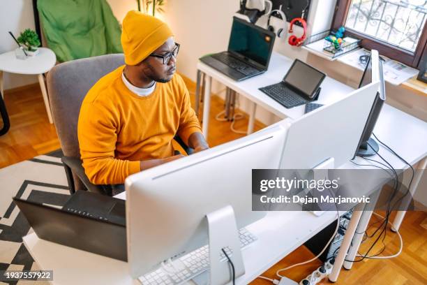 programmer sitting in front of computer screens and working as a freelancer at home settings - web programmer stock pictures, royalty-free photos & images