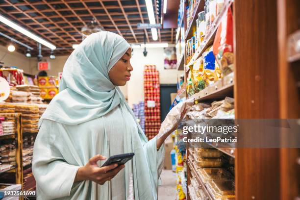 muslim woman consulting shopping list on smart phone - halal stock pictures, royalty-free photos & images