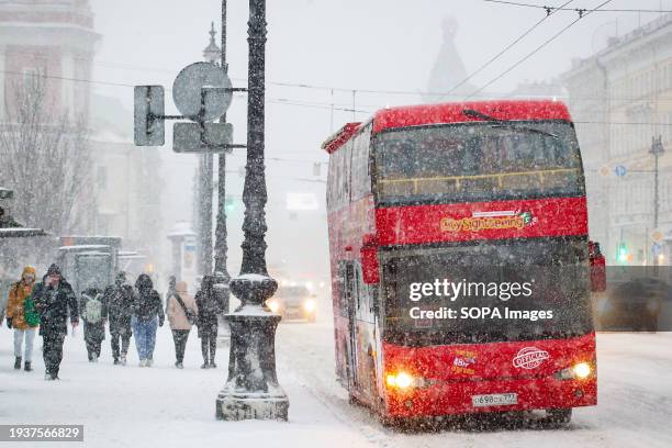 Red tourist bus stands at a bus stop near the Gostiny Dvor metro station during a snowfall in the center of St. Petersburg.