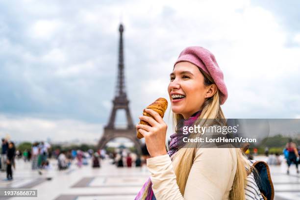 woman eating croissant in front of the eiffel tower in paris - paris street woman stockfoto's en -beelden