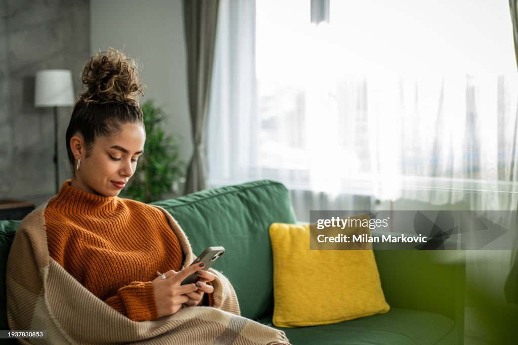 Portrait of cheerful woman using smart phone at home texting or surfing internet