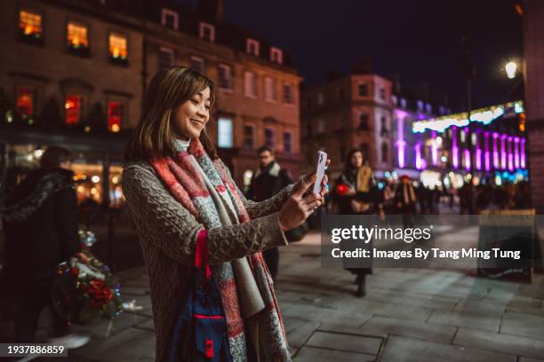 beautiful asian woman making video call with friend on smart phone while walking in city street with christmas lighting in background - virtual event space stock pictures, royalty-free photos & images