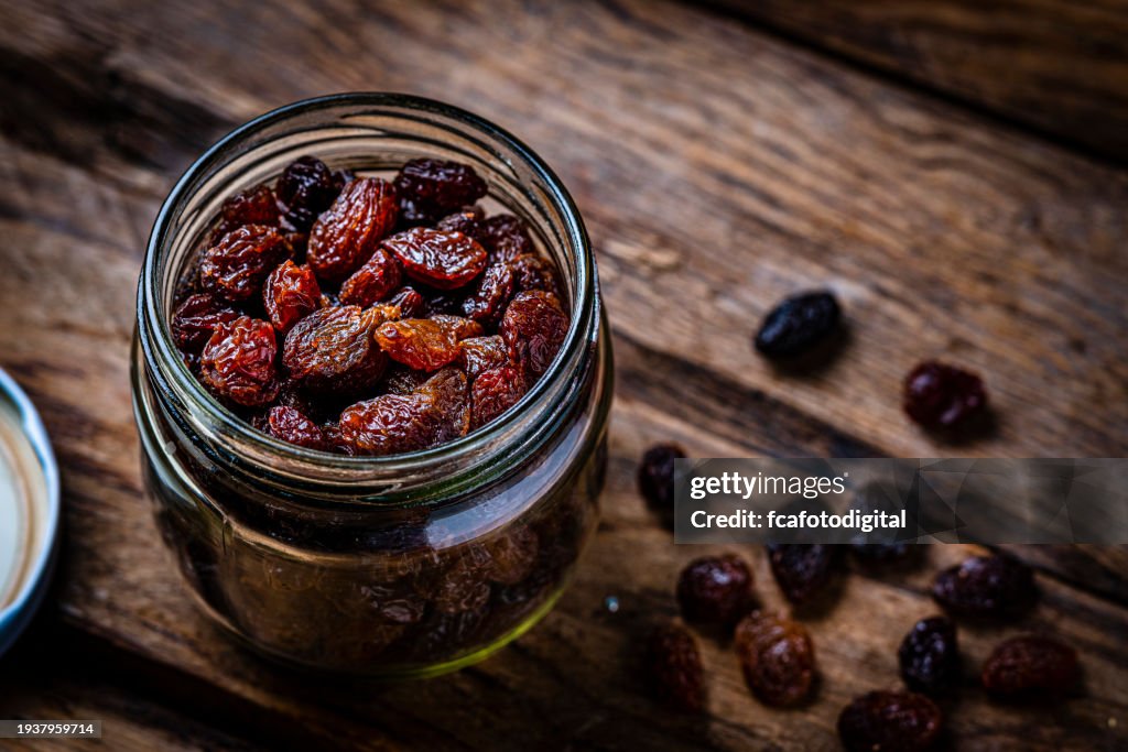 Fresh organic raisins in a glass jar shot on rustic table