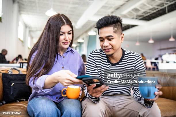young couple exchanging information with smartphones in modern coffeeshop - filipino people stock pictures, royalty-free photos & images