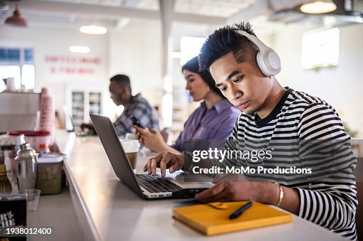 Young man working on laptop with headphones in modern coffeeshop Young man working on laptop with headphones in modern coffeeshop