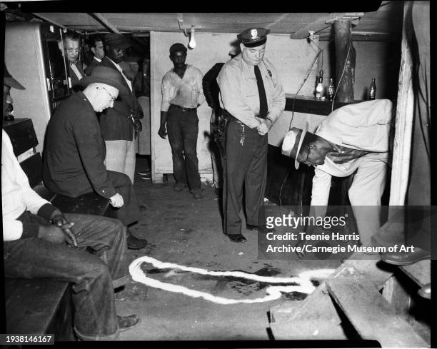 As Assistant Chief of Police Joseph P Devlin watches, murder suspect Theodore Penn leans over a chalk outline beside a bar in the basement of the...