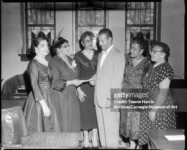 Portrait of Rev Charles H Foggie with a group of five women, including Hattie Matthews as they pose indoors near three stained glass windows,...