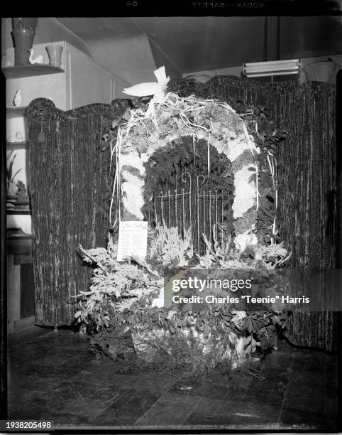 Floral arch memorial with bird on top and crushed velvet curtain in background, Pittsburgh, Pennsylvania, ca 1948. A sign on front reads 'Our Buddy...