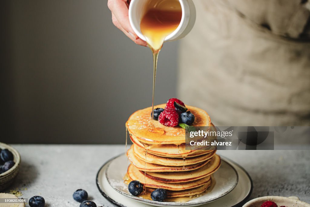 Close-up of woman hand pouring maple syrup over stack of pancakes