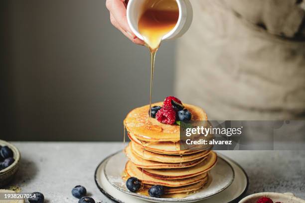 close-up of woman hand pouring maple syrup over stack of pancakes - maple syrup stock pictures, royalty-free photos & images