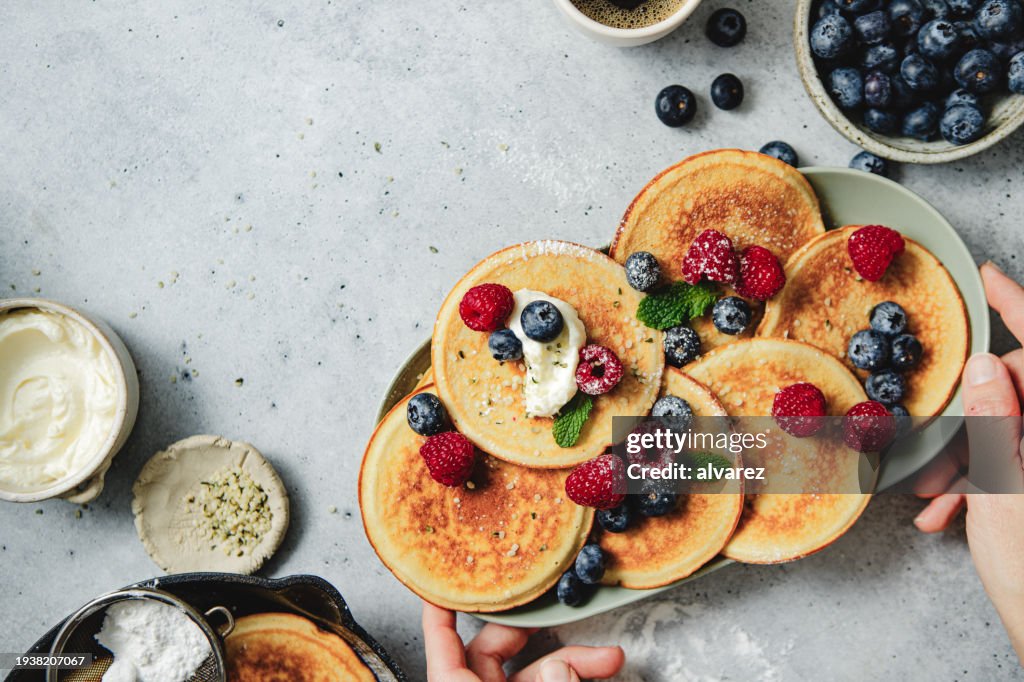 Close-up de mãos de uma mulher servindo panquecas recém-preparadas na mesa