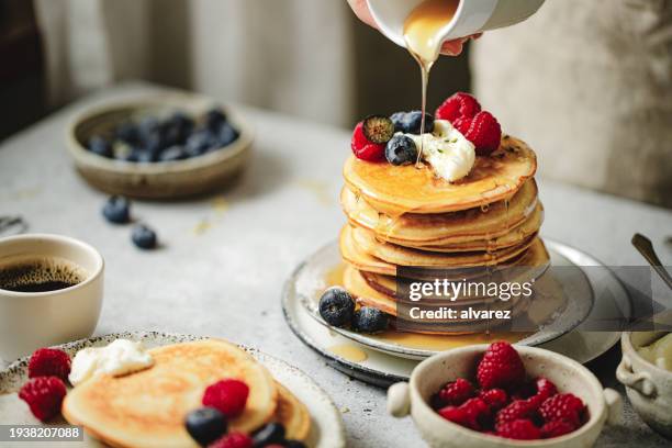 primo piano della donna che versa lo sciroppo d'acero sulla pila di frittelle sul tavolo da pranzo - sciroppo foto e immagini stock