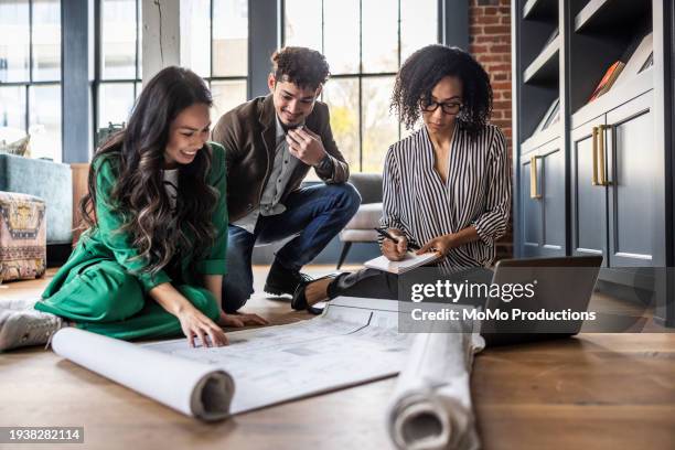 business colleagues looking over building plans on office floor - sit on floor stock pictures, royalty-free photos & images
