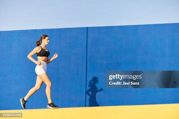 fit runner jogging outside near blue wall - blue shorts stock pictures, royalty-free photos & images