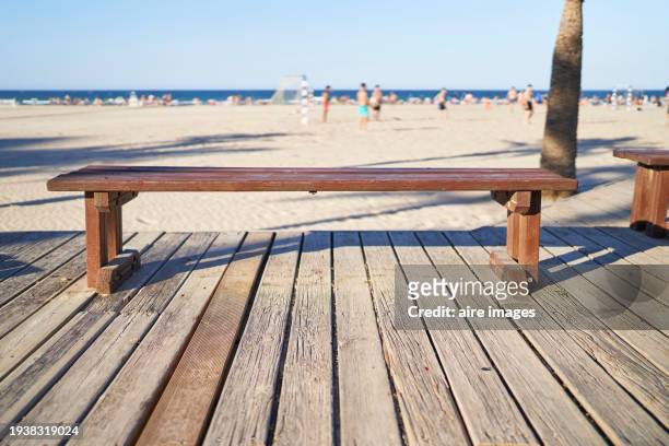 front view of an empty, backless wooden bench on a beach with people in the background - footsteps on a boardwalk bildbanksfoton och bilder