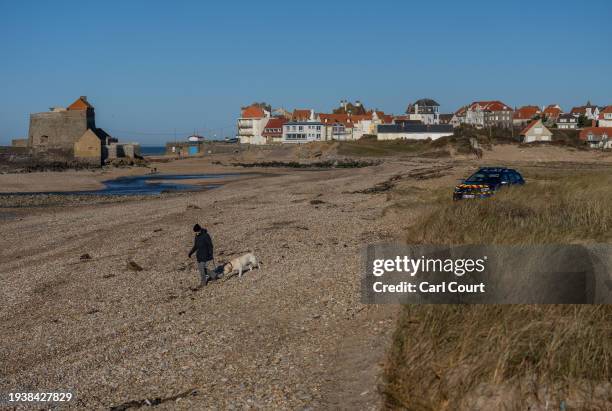 Man walks his dog past a Gendarmes car on a beach known to be used by migrants attempting to cross the English channel, on January 19, 2024 near...