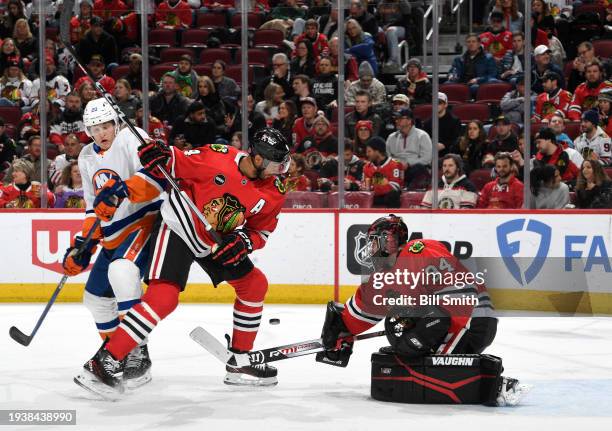 Goalie Petr Mrazek of the Chicago Blackhawks reaches toward the puck as Hudson Fasching of the New York Islanders and Seth Jones of the Chicago...