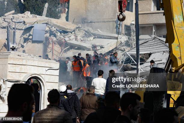 People and rescuers gather in front of a building destroyed in a reported Israeli strike in Damascus on January 20, 2024. An Israeli strike on...