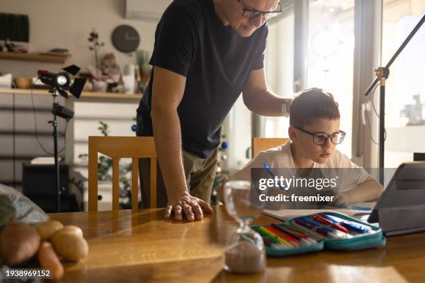 padre devoto ayudando a su hijo con los deberes - hourglass books fotografías e imágenes de stock