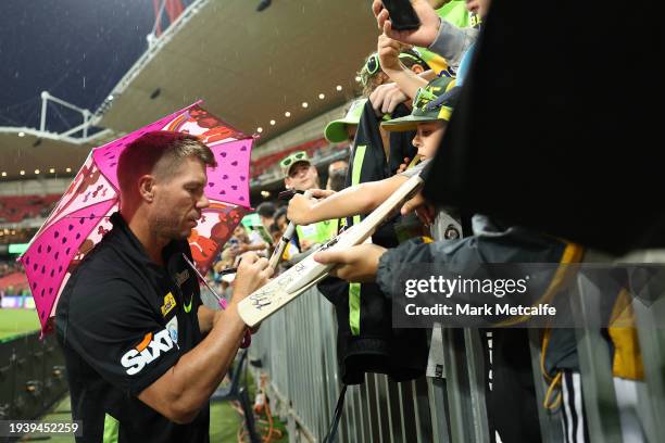 David Warner of the Thunder signs autographs and poses for slefies before the match is abandoned due to rain during the BBL match between Sydney...