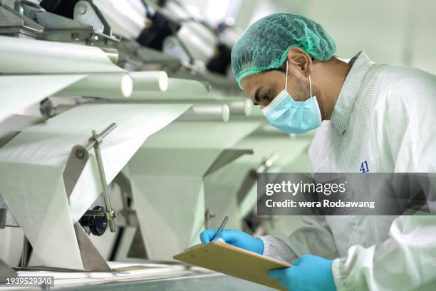 laboratory technician inspecting pharmaceutical manufacturing conveyor belt machine in contaminate controlled room - wearing cloth face mask stock pictures, royalty-free photos & images