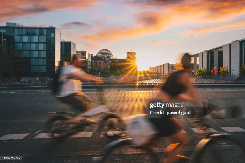 Fahrradpendler passieren das Reichstagsgebäude während des Sonnenuntergangs in Berlin, Deutschland