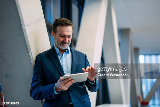smiling businessman using tablet pc near architectural column - geschäftsmann stock-fotos und bilder