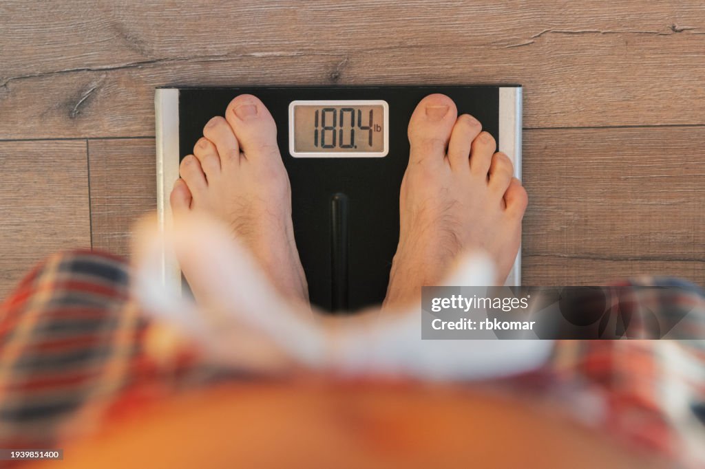 View from Above: Man Weighing In on Scale on Wooden Floor at Home