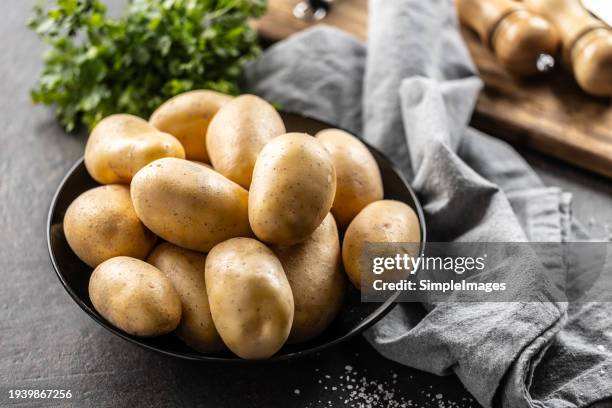 raw potatoes in a black plate on the kitchen table. - pomme de terre photos et images de collection