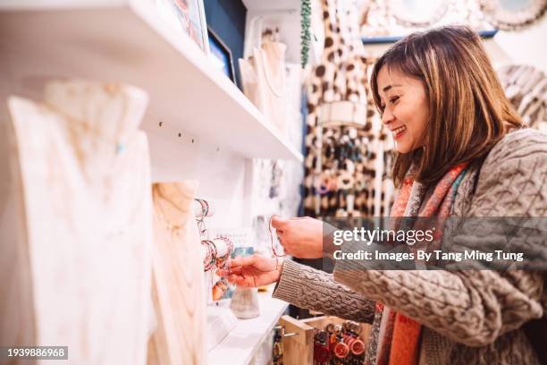 beautiful asian woman shopping for jewellery in an artisan shop during vacation - jewlery store stock pictures, royalty-free photos & images