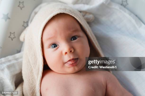 cute boy wrapped in towel and sticking out tongue on bed at home - envuelto en una toalla fotografías e imágenes de stock