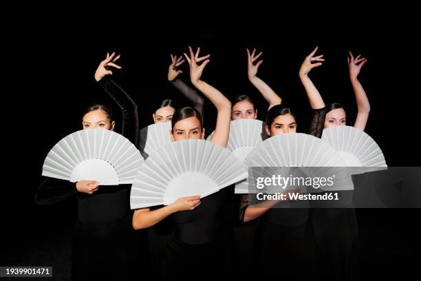 group of flamenco dancers holding hand fans and dancing against black background - flamenco imagens e fotografias de stock