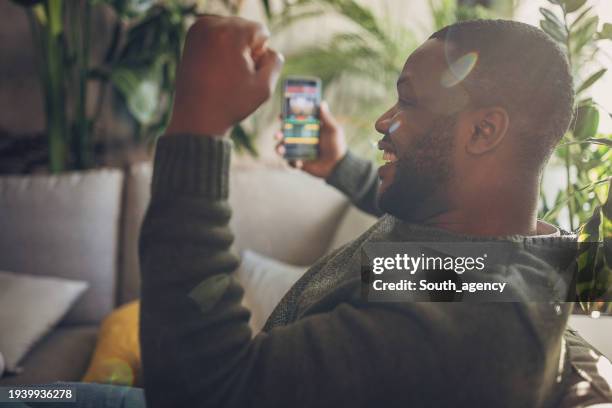 hombre absorto en apuestas deportivas en vivo en un teléfono inteligente - apuestas deportivas fotografías e imágenes de stock