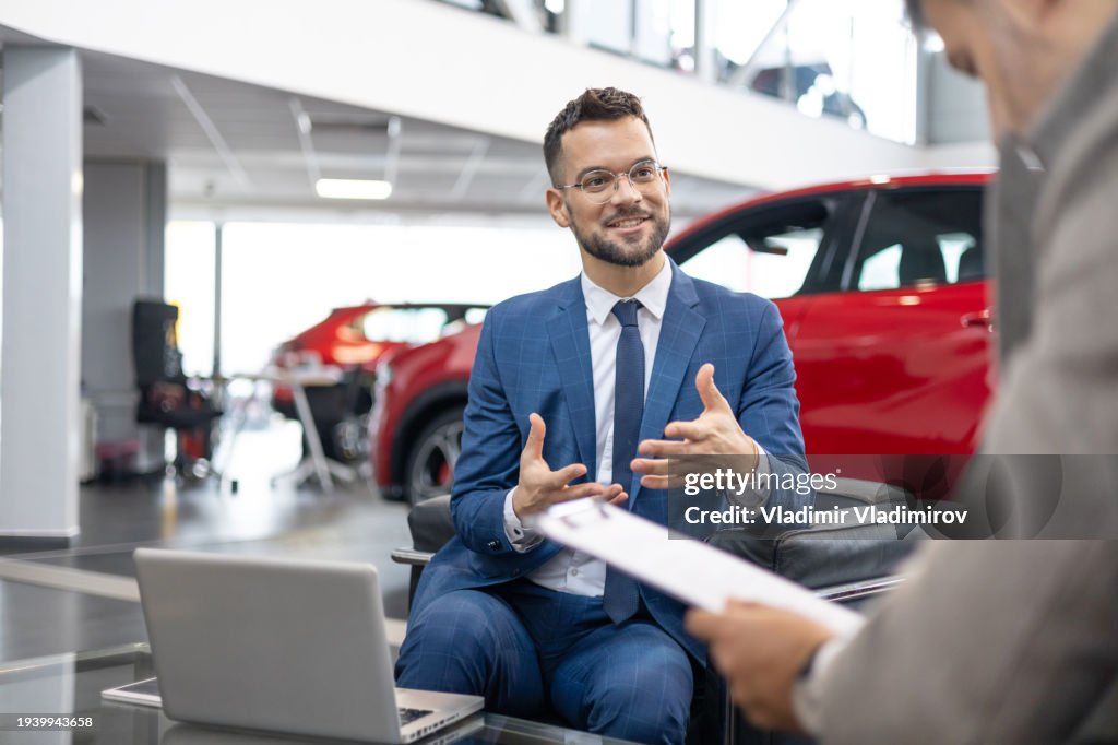 Salesman convincing customer to buy new car Car to Customer at Car Dealership