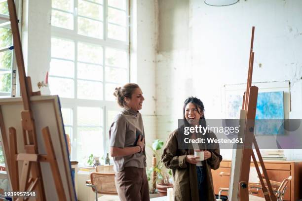 happy women discussing over painting on easel in art studio - maler staffelei stock-fotos und bilder
