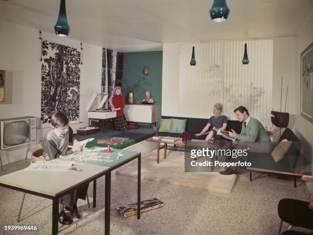 Family group of a man, woman, teenage girl and boy relaxing in the living room of a modern house in England in April 1962. The girl plays records on...
