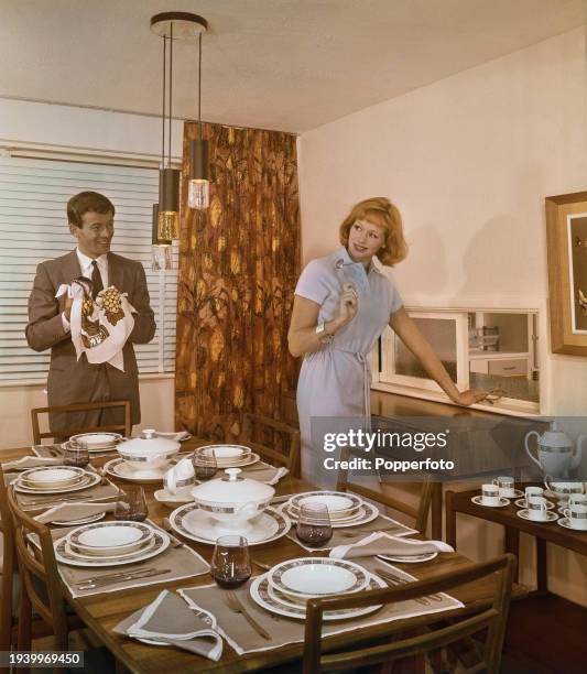 Man and woman clean, prepare and arrange crockery on a table set for six in the dining room of their modern house in England in January 1962. The...